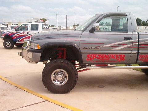 1980 Ford Bronco - Side view of a gray lifted Dodge Ram 2500 V10 regular-cab pickup with red Skyjacker graphics down the door, red suspension components, a ch…