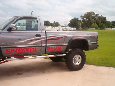 1980 Ford Bronco - Rear 3/4 side view of a gray lifted Dodge Ram 2500 V10 regular-cab long-bed pickup parked on concrete beside a grass field, with red Skyjac…