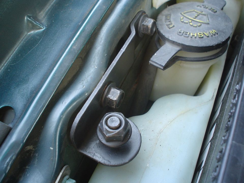 Washer fluid reservoir cap and hood-latch bracket with hex bolts in a green engine bay