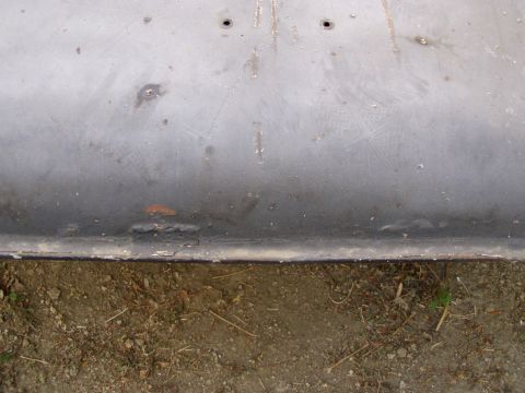 1967 Ford Bronco - Close-up of a gray metal panel with two holes and weld marks, placed on the ground.