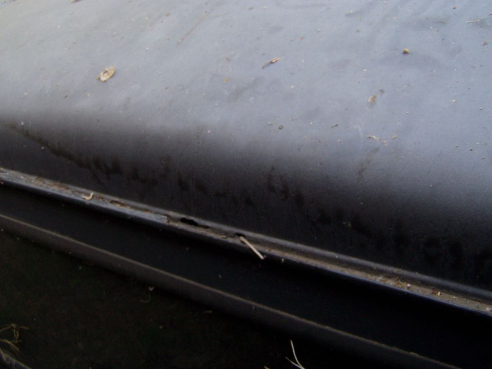Black car body panel showing rust along a seam
