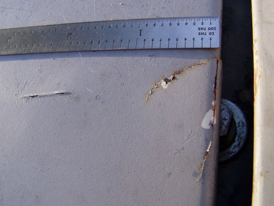 Close-up of a gray metal panel with rust spots and a ruler measuring damage