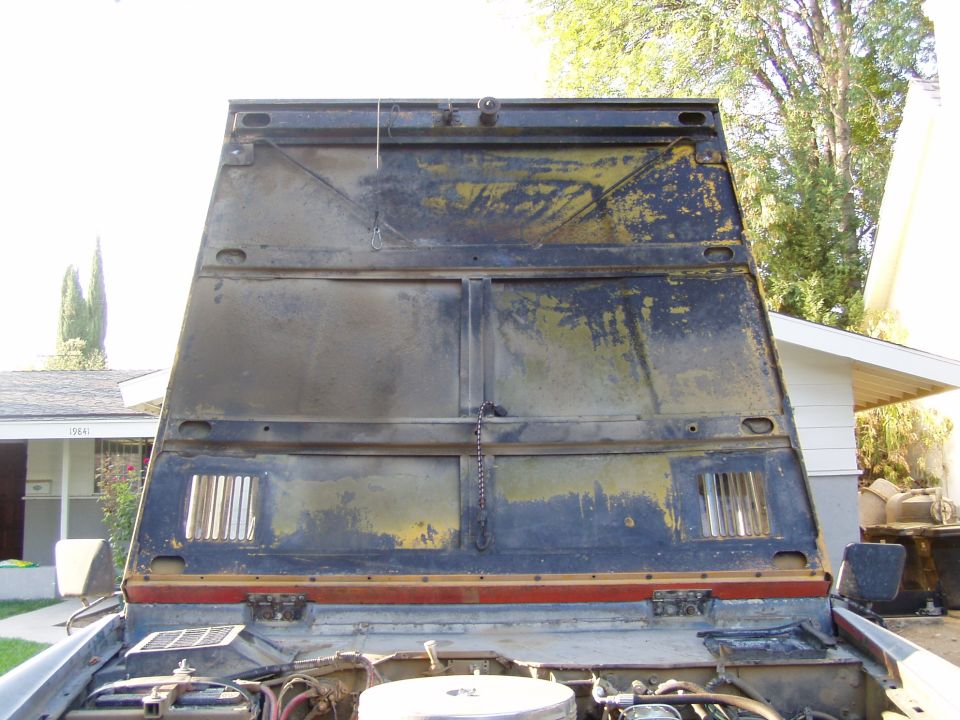 Underside of an open hood with peeling blue and yellow paint and chrome louver vents