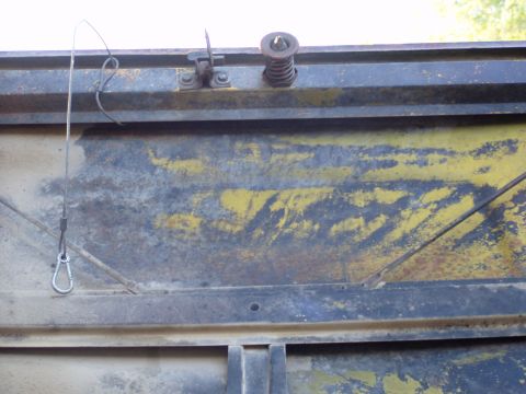 1967 Ford Bronco - Close-up of a rusty metal panel with a spring and latch assembly.