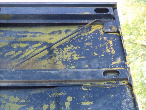 1967 Ford Bronco - Close-up of a weathered tailgate, revealing layers of peeling yellow paint over a blue base, with visible structural elements.