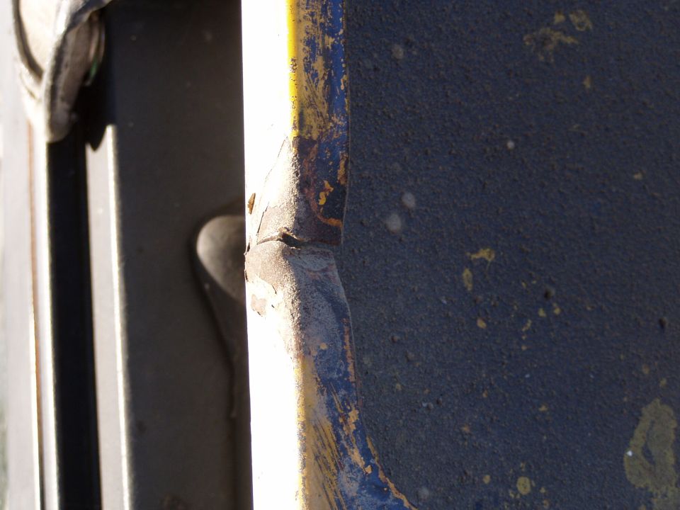 Close-up of a rusted metal edge with blue and yellow paint remnants