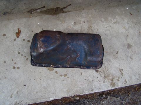 1967 Ford Bronco - A used oil pan sits on a concrete surface, showing signs of age and rust.