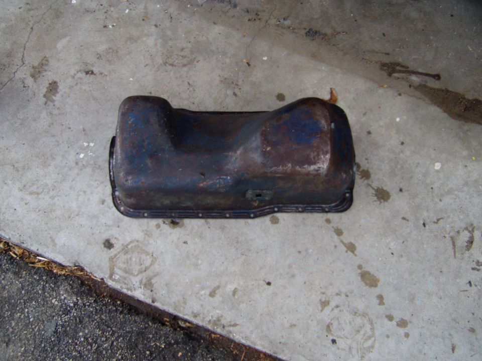 Rusty oil pan on concrete, showing a rectangular cutout and bolt holes along the edge