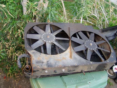 1985 Ford Bronco - This radiator assembly with dual fans is shown outdoors, resting on a green bin.