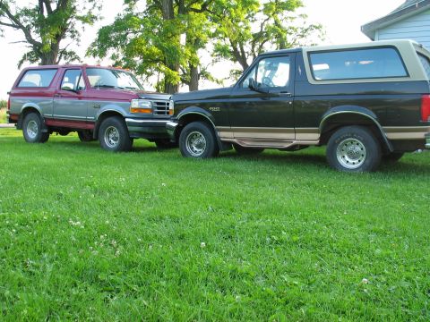 1995 Ford Bronco - Two Ford Broncos, one black and one red and gray, are parked side-by-side on a grassy lawn.