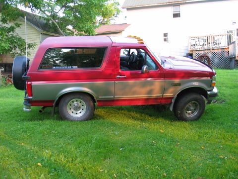 1995 Ford Bronco - This two-tone Ford Bronco is shown from the side, parked on a grassy lawn with houses in the background.