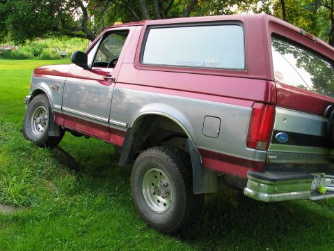 1995 Ford Bronco - This 1995 Ford Bronco features a distinctive red and silver two-tone paint scheme and is parked on a grassy area.