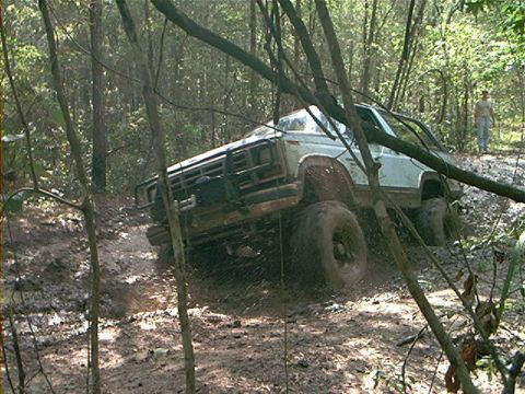1986 Ford Bronco - This 1986 Ford Bronco is navigating a challenging muddy terrain in a wooded area.