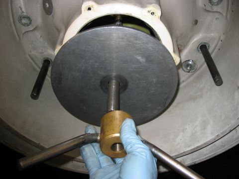 1988 Ford Bronco - A gloved hand operates a tool on a threaded rod attached to a large metal disc, part of a mechanical assembly.
