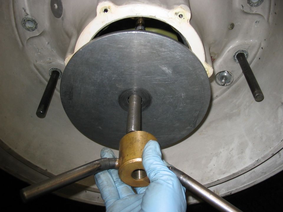 Close-up of a mechanical part with a threaded rod and a brass tool being operated by a gloved hand