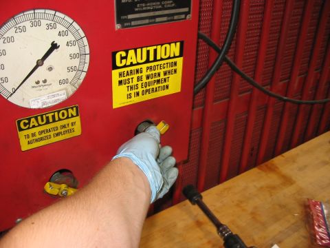 1988 Ford Bronco - Gloved hand operates a knob on red equipment with caution labels and a large gauge.