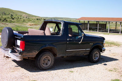 1995 Ford Bronco - A dark green 1992 Ford Bronco is parked on a gravel lot with a picnic shelter in the background.