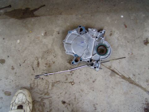 1985 Ford Bronco - A vehicle part, likely an engine timing cover, is shown on a stained concrete surface.