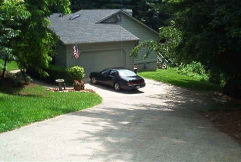 1985 Ford LTD Crown Victoria - A dark sedan is parked in a driveway in front of a garage, viewed from the rear.
