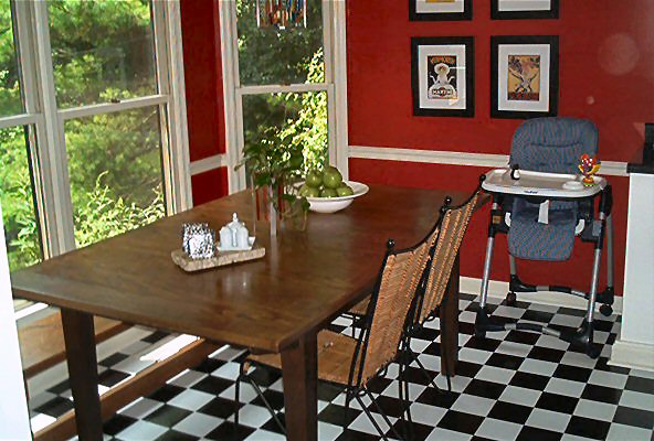 Dining room with a wooden table, chairs, and a high chair, set against red walls and a checkered floor