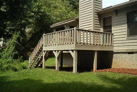 1985 Ford LTD Crown Victoria - Exterior view of a house a wooden deck and stairs, surrounded by grass and trees.