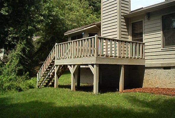 Wooden deck with stairs attached to a house with vinyl siding and a brick foundation