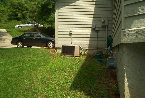 Dark sedan parked on grass, white sedan on driveway behind it. Both appear to be from the 1980s