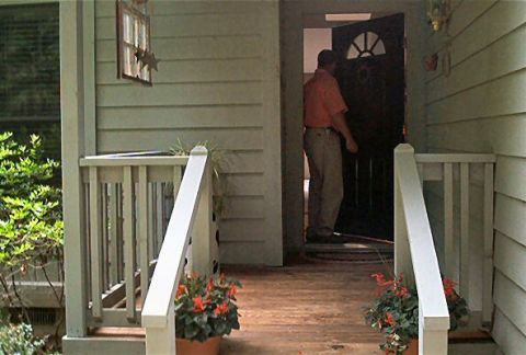 1985 Ford LTD Crown Victoria - A man enters a home through the front door on a wooden porch with railings and potted flowers.