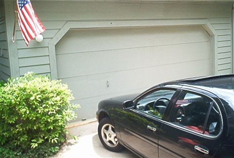 1985 Ford LTD Crown Victoria - Side view of a black sedan parked in front of a garage door with an American flag.