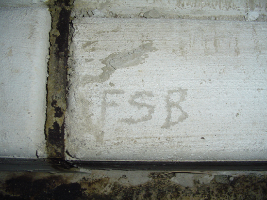 Concrete wall with "FSB" faintly written on it, showing water stains and a dark seam