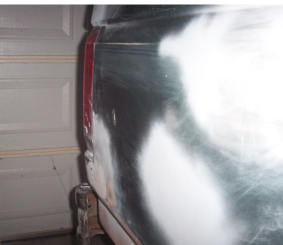 Sanded and filled rear corner bodywork on a dark green truck in a garage