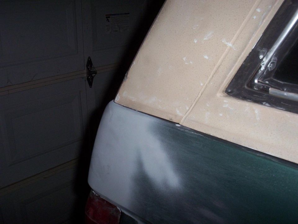 Green SUV rear quarter sanded to primer during bodywork below a tan hardtop