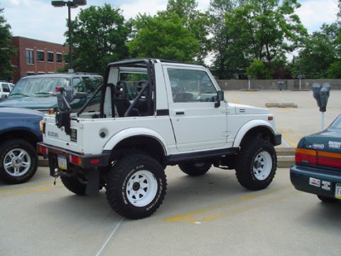 1979 Ford Bronco - A white Suzuki Samurai is parked in a lot, showing its lifted suspension and off-road tires.