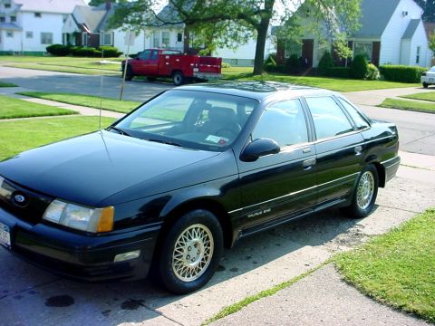 1989 Ford Taurus - A black 1989 Ford Taurus sedan is parked on the side of a residential street.