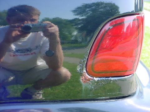 1989 Ford Taurus - Rear taillight shows damage and rust. Photographer is visible in the reflection.