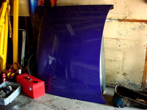 1989 Ford Taurus - A single purple car hood is shown leaning against a wall in what appears to be a garage or workshop.
