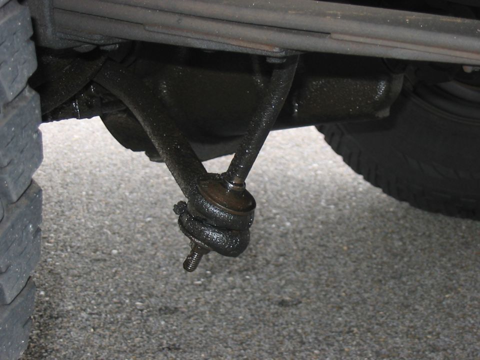 Close-up of greasy steering linkage and tire tread on asphalt