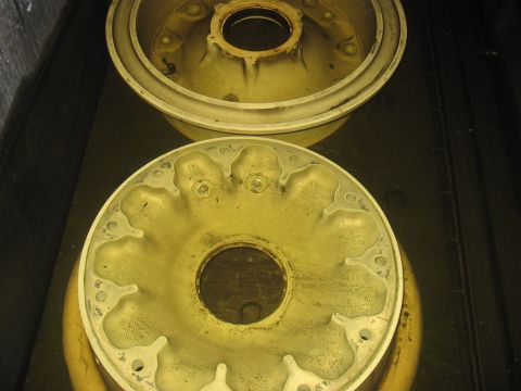 1988 Ford Bronco - Two yellowed metal wheel hubs are shown, one stacked on top of the other, in this close-up view.