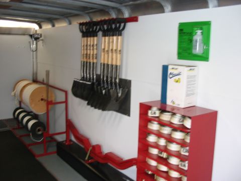 1988 Ford Bronco - A storage area is organized with tools, including shovels and rope spools, alongside a red shelving unit containing various items.
