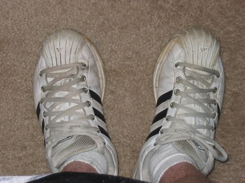 1988 Ford Bronco - White Adidas sneakers with black stripes are shown from a top-down perspective on a carpeted surface.