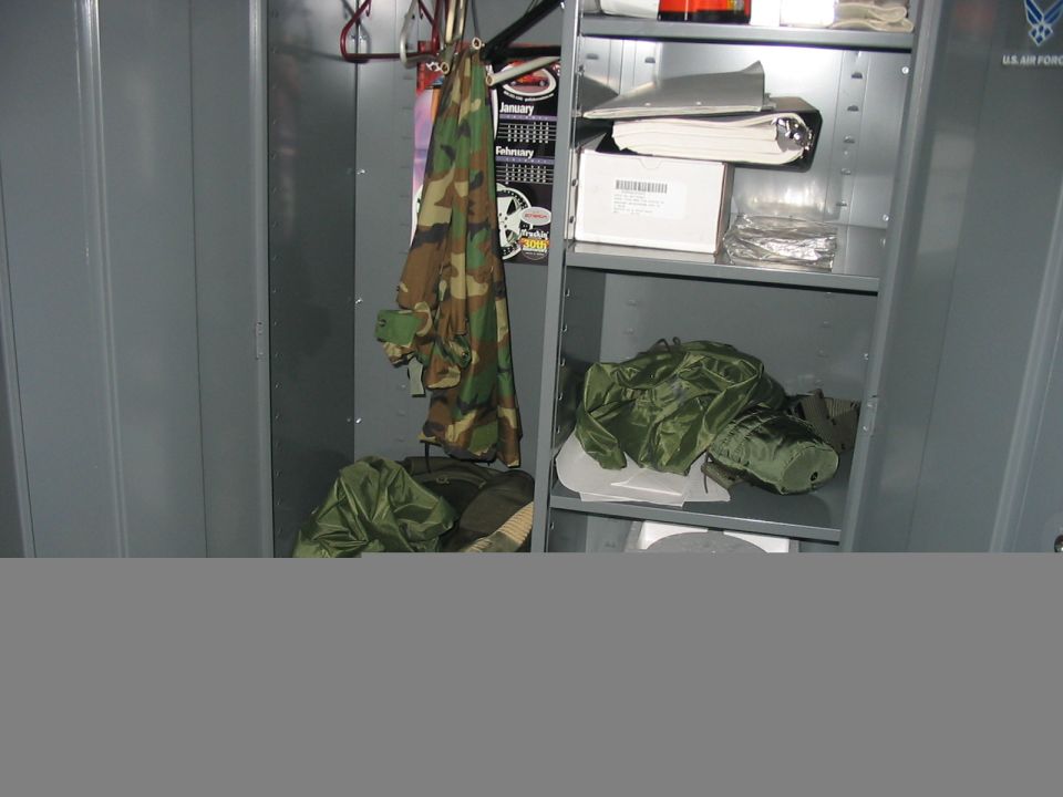 Interior of a gray metal locker containing camouflage jackets, green bags, and stacked papers