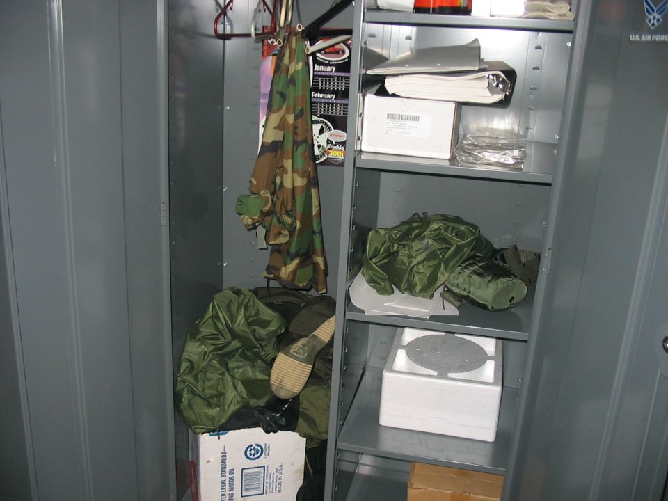 Interior of a gray metal locker filled with camouflage clothing and green bags