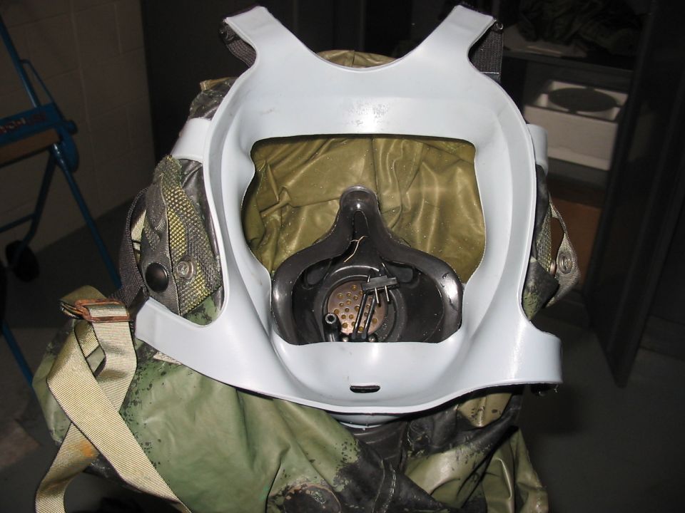 Gas mask with white plastic face shield over olive drab and camouflage protective suit