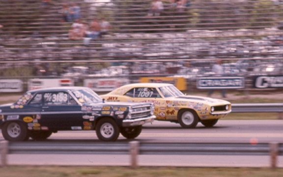 Dark blue and yellow vintage drag cars racing side by side on a track