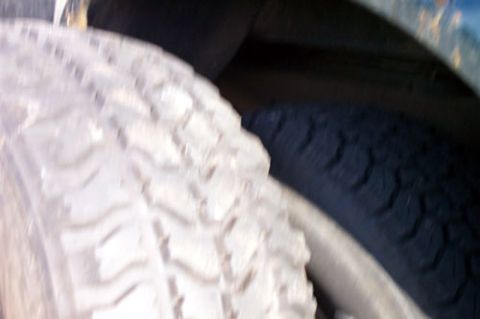 1995 Ford Bronco - Blurry extreme close-up of an aggressive mud-terrain tire tread and sidewall, with a second tire visible behind it in the shadows. The chun…