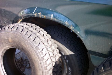 1995 Ford Bronco - Close-up comparison of two tires leaning against the rear fender of a dark green truck, showing an aggressive all-terrain tread block patte…