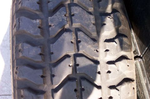 1995 Ford Bronco - Close-up of the tread on a mud-terrain tire, showing large staggered chevron lugs with moderate wear, photographed in sunlight against a da…
