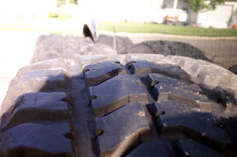 1995 Ford Bronco - Extreme close-up along the tread face of a mud-terrain tire, showing the deep chunky lugs, siping and molded stone-ejector nubs between blo…