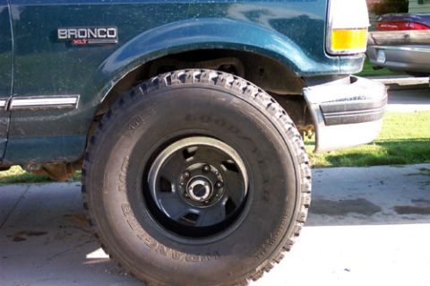 1995 Ford Bronco - Close-up of the front wheel and fender of a teal-green Ford Bronco XLT on a driveway, showing a Goodyear Wrangler MT/R mud-terrain tire on…