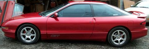 1996 Ford Probe - The side profile of a red 1996 Ford Probe GT is captured with its doors ajar, revealing the interior.
